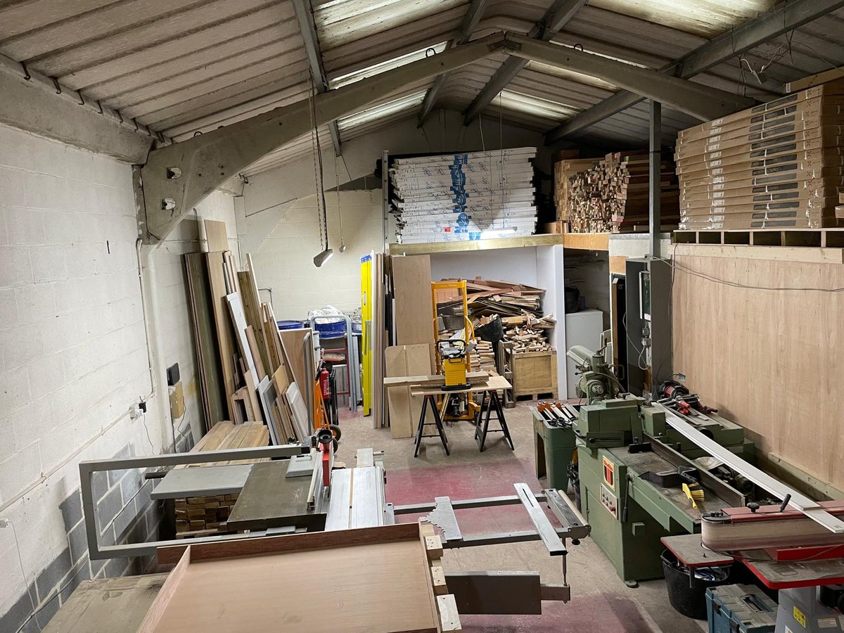 Cluttered workshop interior with construction materials, wooden boards, tools, storage shelves, and work station organized throughout the space
